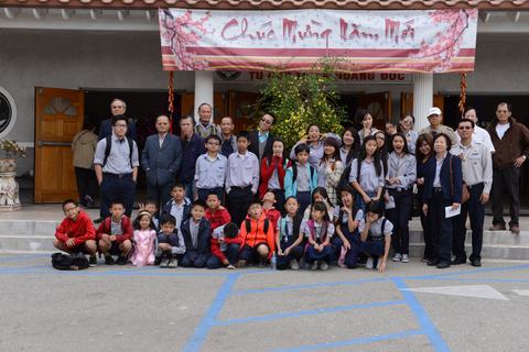 Các em lớn và phụ huynh đứng hàng sau, băng-rôn đỏ và dây pháo trên cột