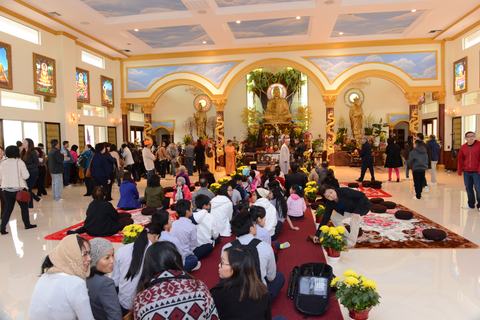 Chánh điện nhìn rộng, tôn tượng Phật vàng dưới vòm, Phật tử đi lại, các em ngồi giữa