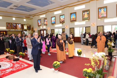 Cả chánh điện đứng chắp tay, người lớn và các em, hoa cúc vàng và thảm đỏ