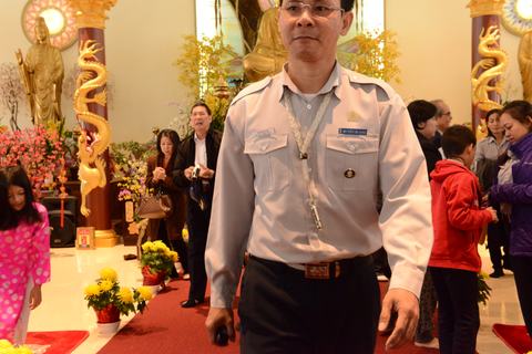 Một anh Huynh Trưởng trong đồng phục áo lam đứng giữa chánh điện, hoa cúc vàng bên cạnh