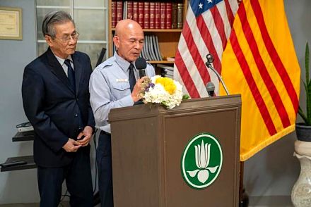 Hai huynh trưởng phát biểu tại bục có phù hiệu Hoa Sen, bên cạnh cờ Hoa Kỳ và cờ vàng
