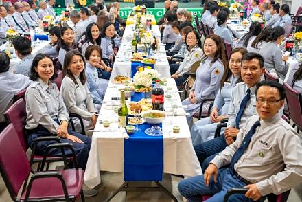 Các huynh trưởng ngồi quanh bàn tiệc, phía sau là cờ và phông sân khấu