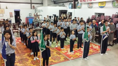 Hàng đoàn sinh Ngành Thiếu chắp tay, cờ đoàn xanh lá phía sau