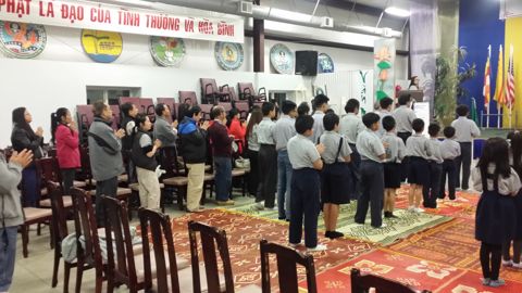 Phụ huynh đứng cuối hội trường chắp tay, nhìn về phía các em và bàn Phật