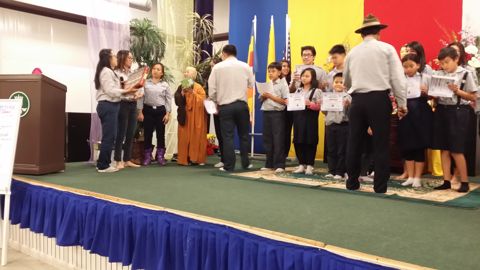 Sư Cô Tịnh Ngọc trên sân khấu trao chứng chỉ cho một em đoàn sinh, các em khác cầm bằng đứng hai bên