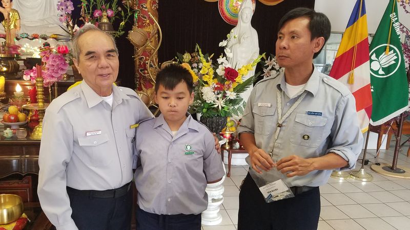 Hai Huynh Trưởng đứng cùng một em Oanh Vũ trước bàn thờ Phật