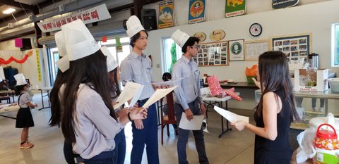 Ba em Ngành Thiếu đội mũ giấy, cầm tờ giấy đọc trước giờ nấu