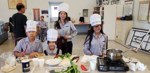 Đội Chef Hà Nội ngồi trước bàn với nồi và rau, hai em nhỏ ngồi hàng đầu cười tươi