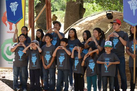 Đội Freljord, các em nhỏ nhất, làm dấu trái tim bằng hai tay trước cổng trại, hai anh chị lớn cầm cờ hiệu hai bên