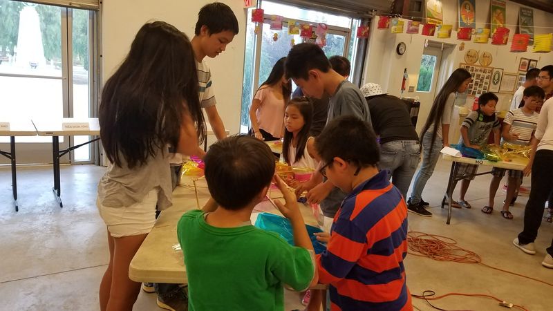 Một em nhỏ cầm khung lồng đèn trong khi người lớn dán giấy kiếng